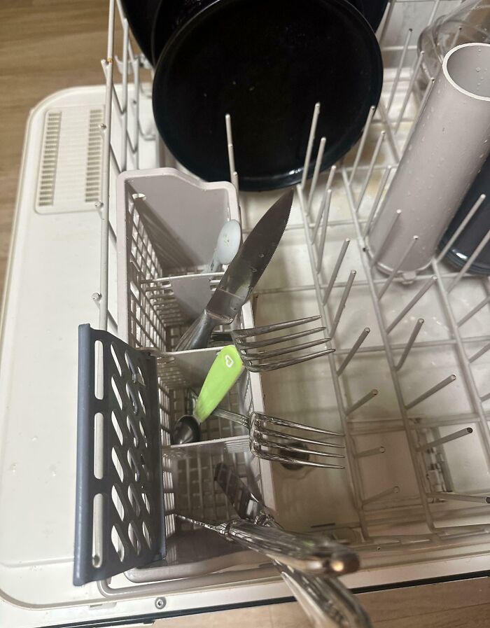 Cutlery placed incorrectly inside a dishwasher, illustrating clueless partners struggling with basic dishwasher loading.