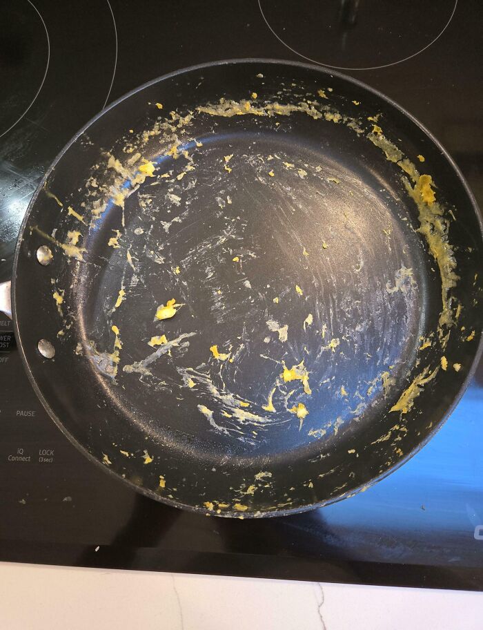 Nonstick frying pan with burnt and stuck scrambled eggs, illustrating clueless partner cooking fail humor.