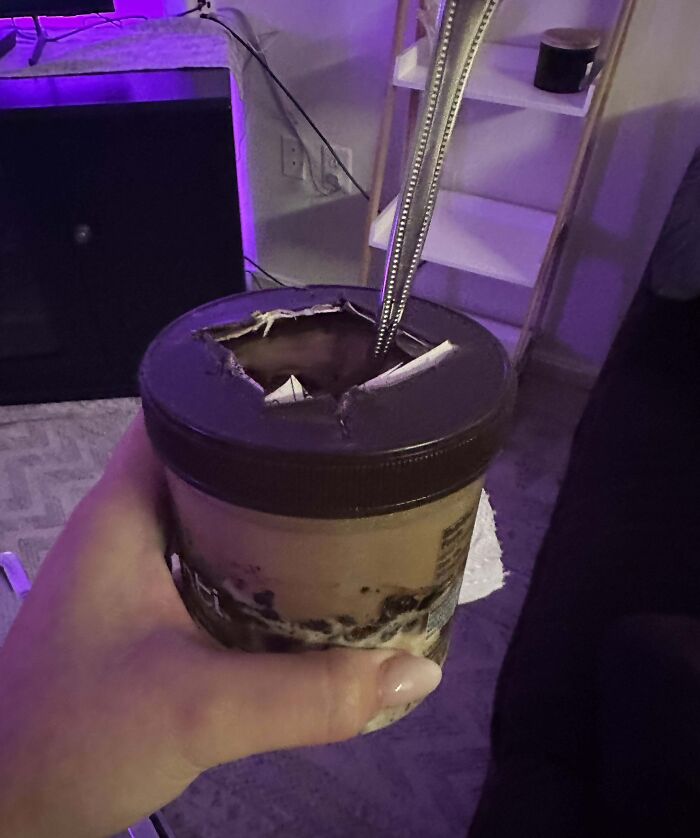 Hand holding ice cream with a lid punctured by a spoon, a hilarious photo showing clueless partners in action.