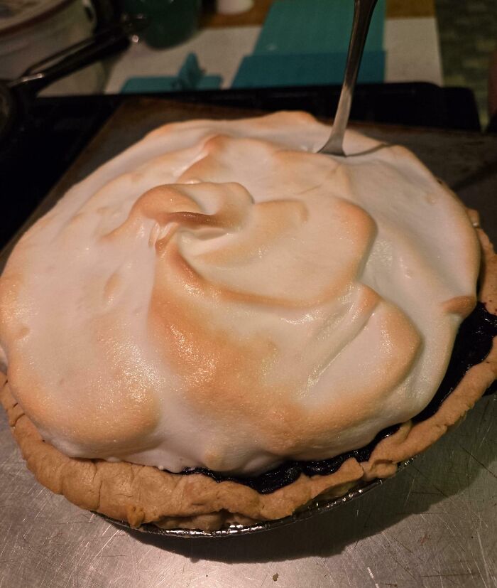 Meringue pie with unevenly browned topping and a fork stuck awkwardly in the dessert, showing clueless partner cooking fail.