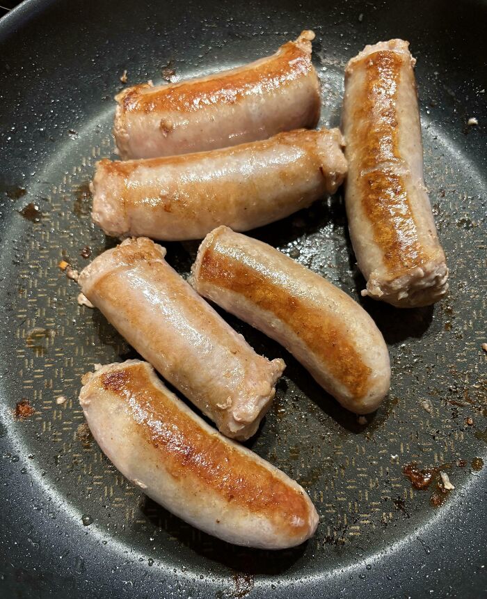 Six sausages frying unevenly in a pan, illustrating clueless cooking skills of some people's partners.
