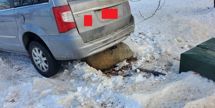 Silver car stuck on a large rock in the snow, illustrating clueless partners in a hilarious mishap.