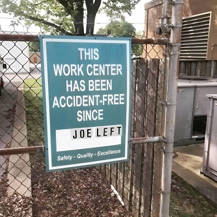 Funny work meme sign on a fence stating the work center has been accident-free since Joe left, humor at the workplace.