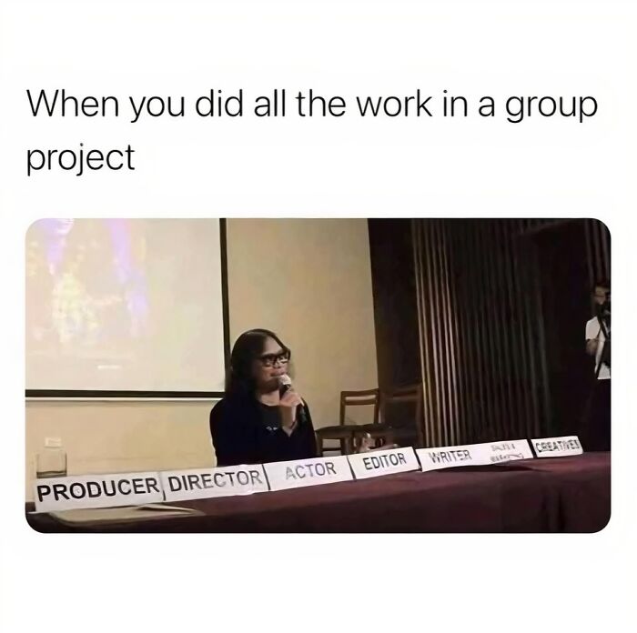 Person sitting alone behind multiple roles signs, representing doing all work in a group project, funny work memes concept.
