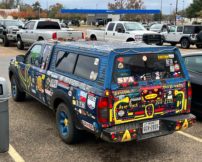 Old pickup truck in a parking lot covered with outrageous car mods and colorful custom decals and artwork.