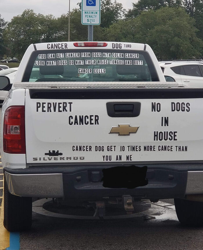 White Chevrolet Silverado truck with controversial, large text stickers about cancer and dogs on rear windshield and tailgate, outrageous car mods.