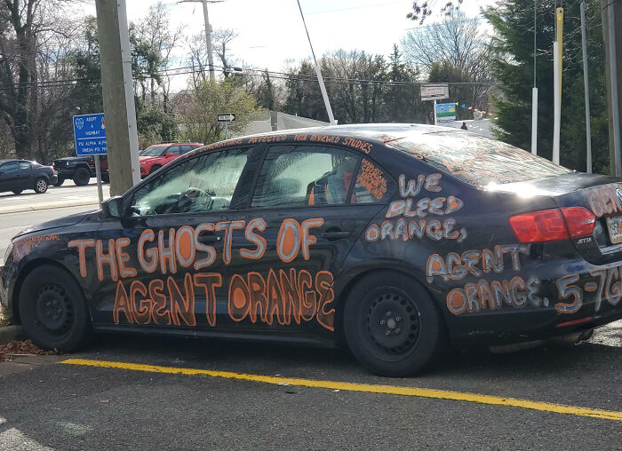 Black car with outrageous custom orange graffiti covering its body, showcasing extreme car mods that took things way too far.
