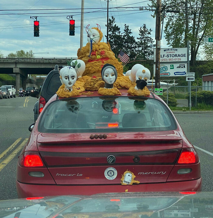 Red Mercury Tracer car with bizarre outrageous car mods featuring multiple mannequin heads and unusual decorations on the roof.