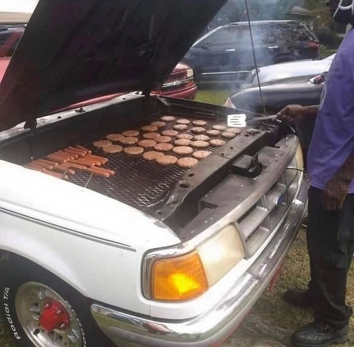 Grilling burgers and hot dogs on a car engine grill, a creative and blessed outdoor cooking setup.