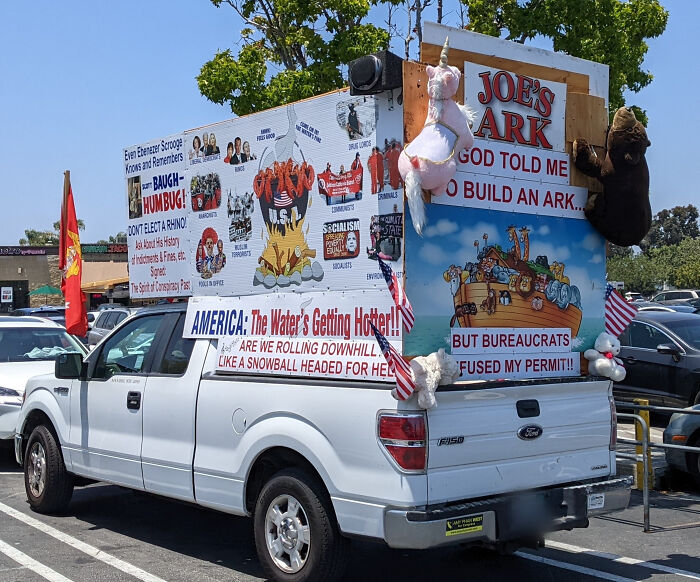 White truck with an outrageous car mod featuring large political and social signs, stuffed animals, and flags on the back.