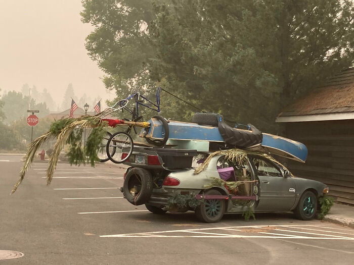 Vintage car heavily modified with a boat, bicycle, branches, and various items in an outrageous car mods style.