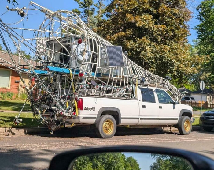 White pickup truck with outrageous car mods featuring an elaborate metal frame and solar panel on a residential street.
