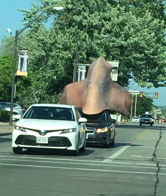 Black car with an outrageous car mod featuring a giant nose attachment driving behind a white car on a city street.