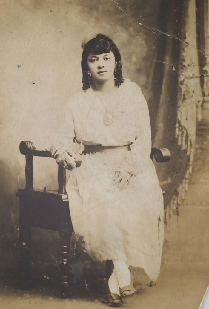 Vintage postcard portrait of a woman from the 1930s seated on a wooden chair in a classic studio setting.