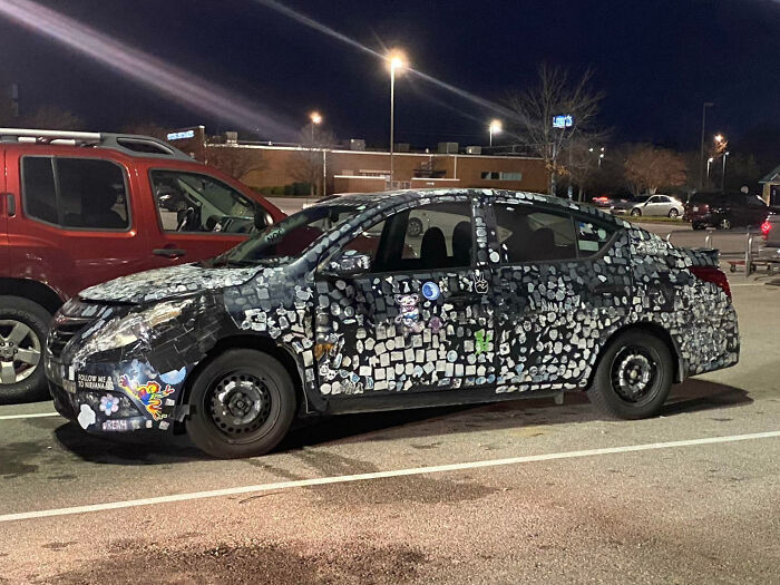 Car covered with numerous stickers parked at night, showcasing one of the outrageous car mods that took things way too far.