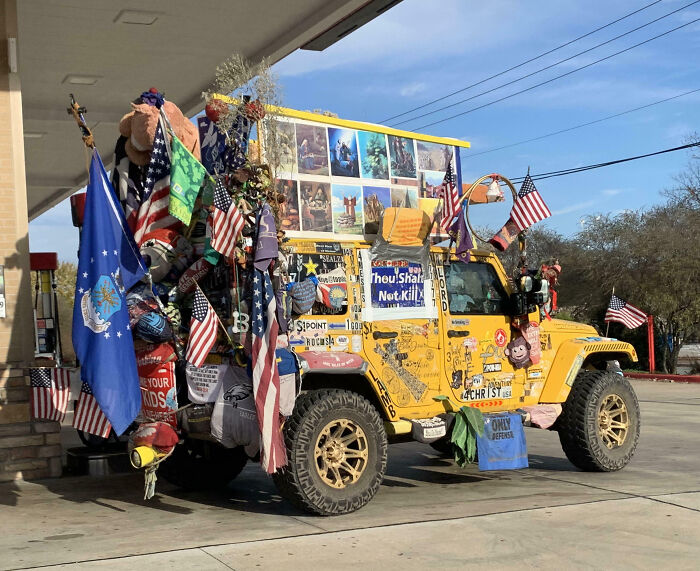 Yellow off-road vehicle with numerous outrageous car mods including flags, stuffed animals, and signs covering the exterior.