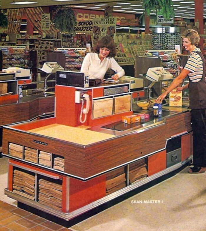 Vintage grocery store checkout from the 1970s with cashier and customer amid retro store displays and products.