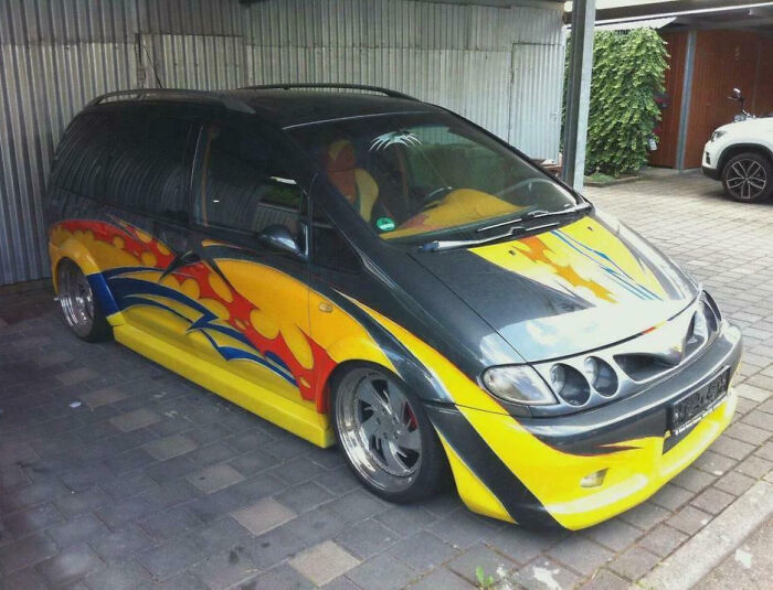 Modified compact car with custom lowered body, vibrant flame decals, and unique multi-headlight design parked in a garage.