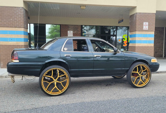 Black sedan with oversized gold rims parked in front of a building, showcasing outrageous car mods that went way too far.