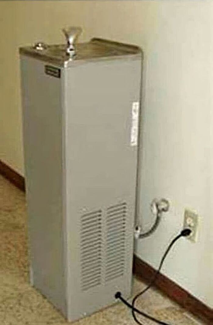 Vintage water fountain from the 1980s with a metal spout and plugged-in electrical cord in a carpeted room