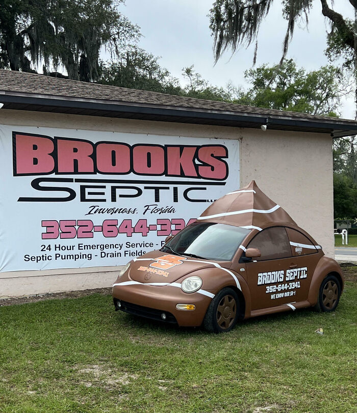 Brown Volkswagen Beetle with an outrageous septic tank themed car mod parked on grass near a business sign in Florida.