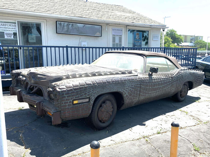 Outrageous car mod featuring an alligator-style textured exterior covering a vintage convertible parked outside a shop.