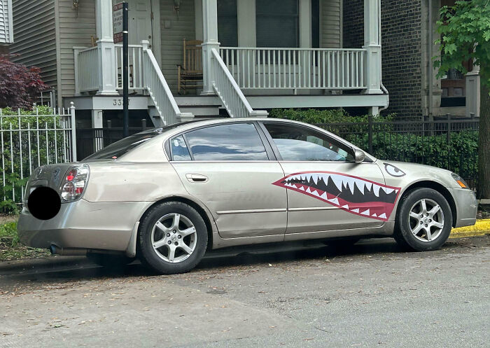 Silver sedan with outrageous car mods featuring shark mouth decals on the side, parked on a city street near a house.