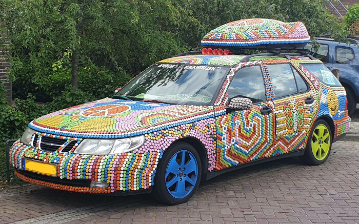 Car covered in colorful bottle cap mods with mismatched blue and yellow wheels, showcasing an outrageous car mod design.