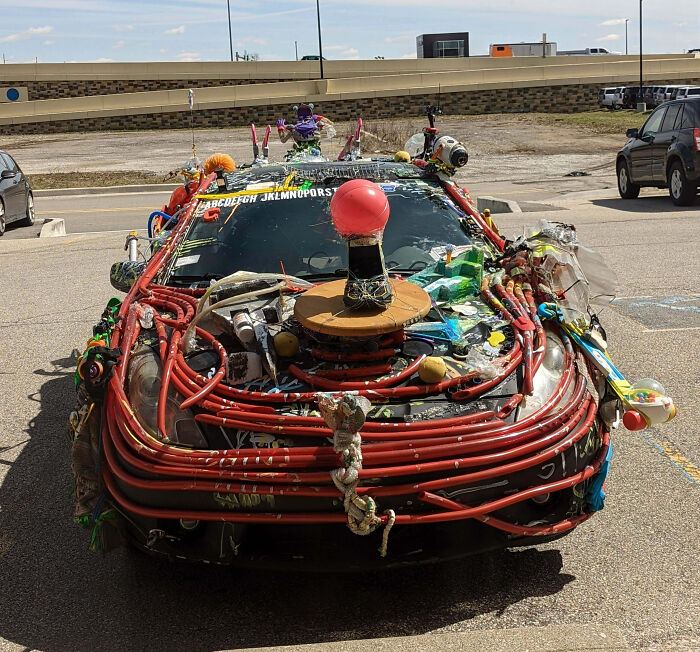 A car covered in outrageous car mods including colorful pipes, toys, and various objects making it look chaotic and unique.