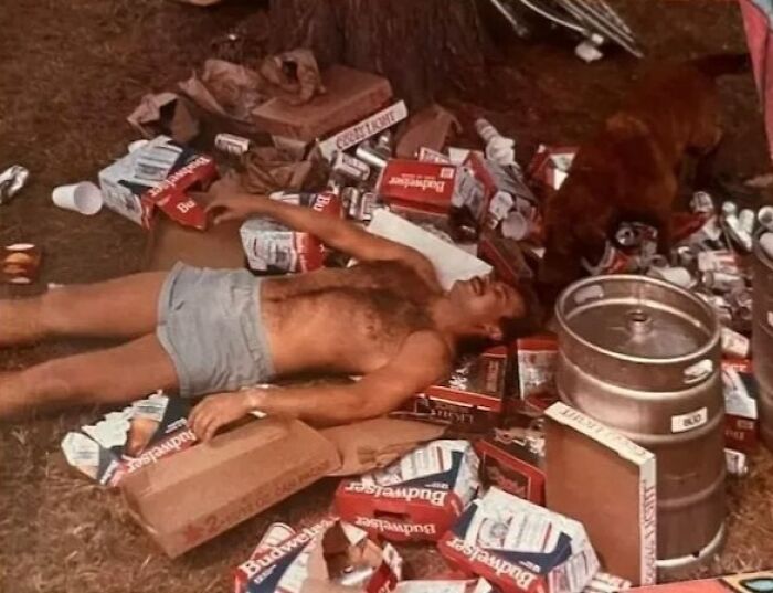 Vintage photo of a dad embodying old school cool, lying among beer boxes and a keg outdoors.
