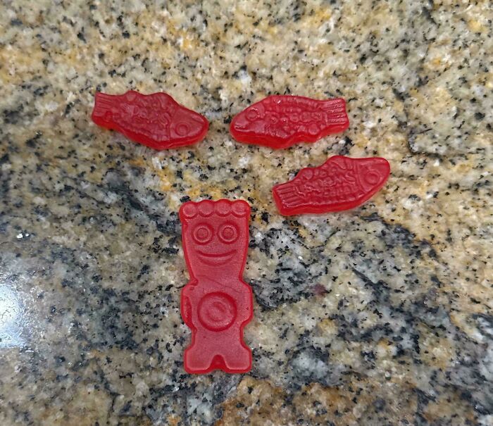 Red candy shaped like three fish and a smiling figure, showcasing a mildly interesting and unique arrangement on a granite surface.