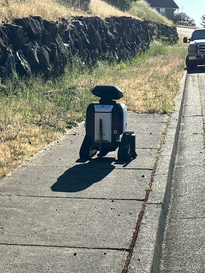 Small robot on sidewalk with wheels casting shadow on a sunny day, an example of something mildly interesting to share.