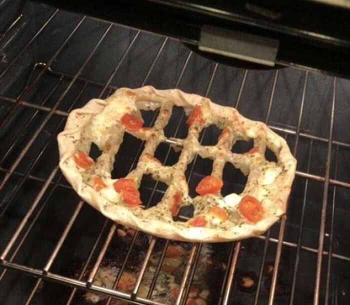 Bizarre cursed food picture showing a misshapen pizza crust with sparse toppings baking inside an oven rack.