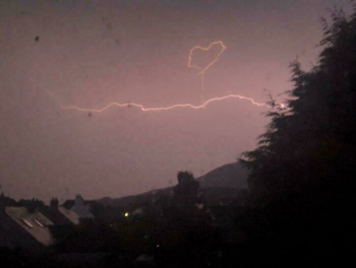 Lightning forming a heart shape in the sky above a dark landscape, a mildly interesting natural phenomenon shared online.