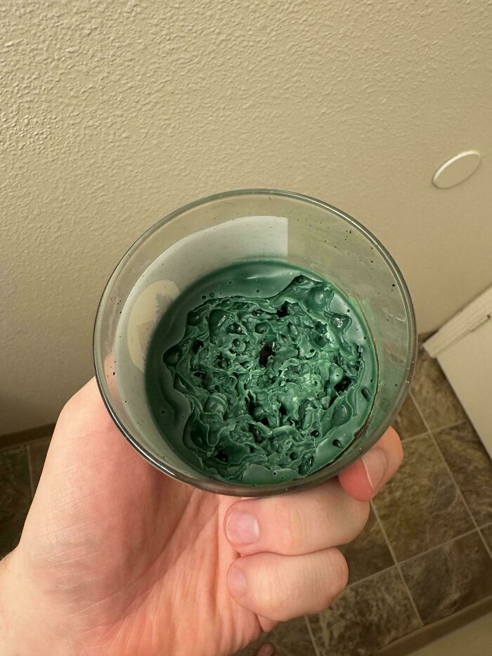 Hand holding a glass with dried green paint inside, showing mildly interesting texture patterns and details.
