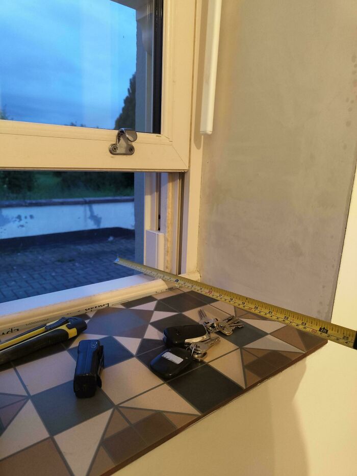 Measuring a window with tools and keys on patterned tiles, showcasing a mildly interesting DIY setup.
