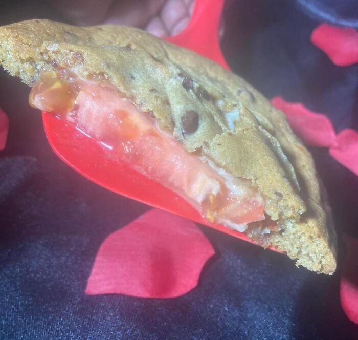 Close-up of a chocolate chip cookie with a slice of tomato inside, a cursed picture of food that might make you go eeeeeuw