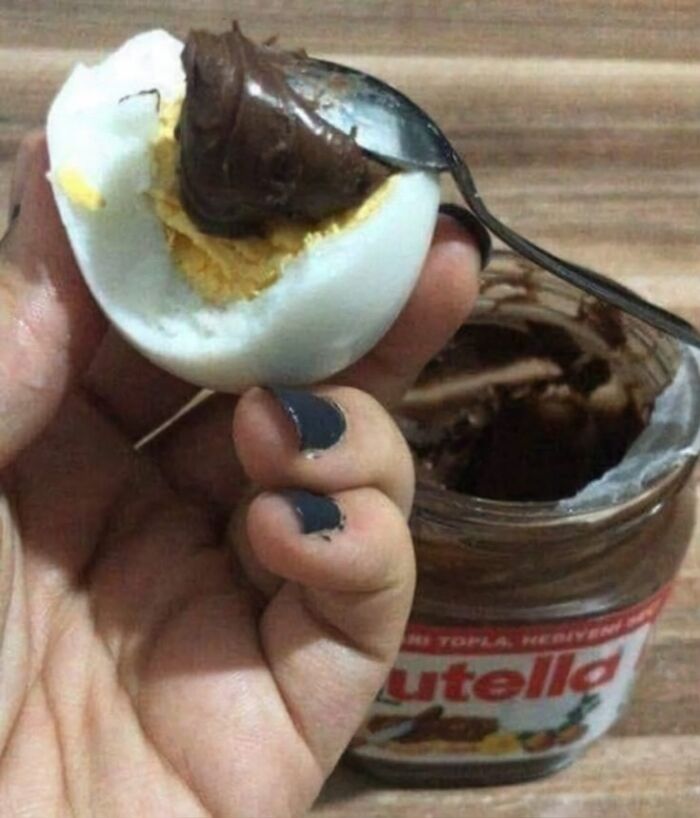 Hand holding a hard-boiled egg smeared with Nutella chocolate spread, a unique and cursed picture of food.