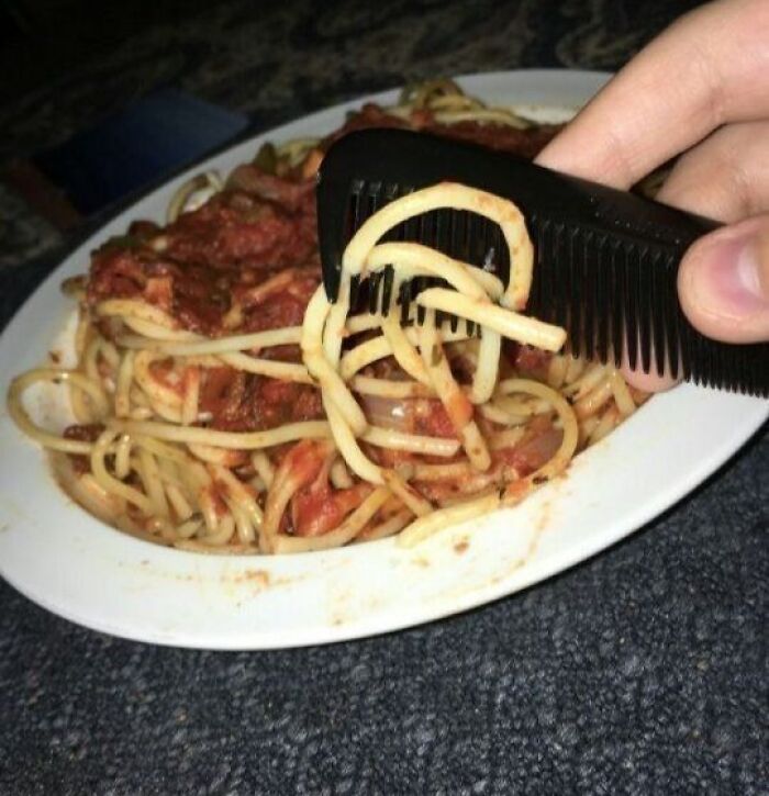 Plate of spaghetti with red sauce being eaten using a black comb instead of a fork, a cursed food picture.