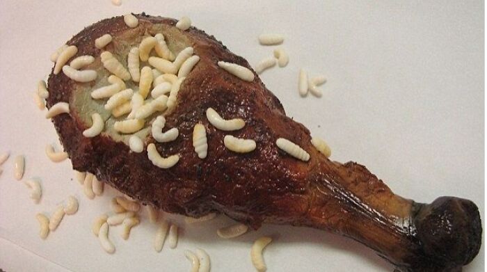 Rotten chicken drumstick covered with white maggots on a white surface, a cursed picture of food that might disgust viewers.