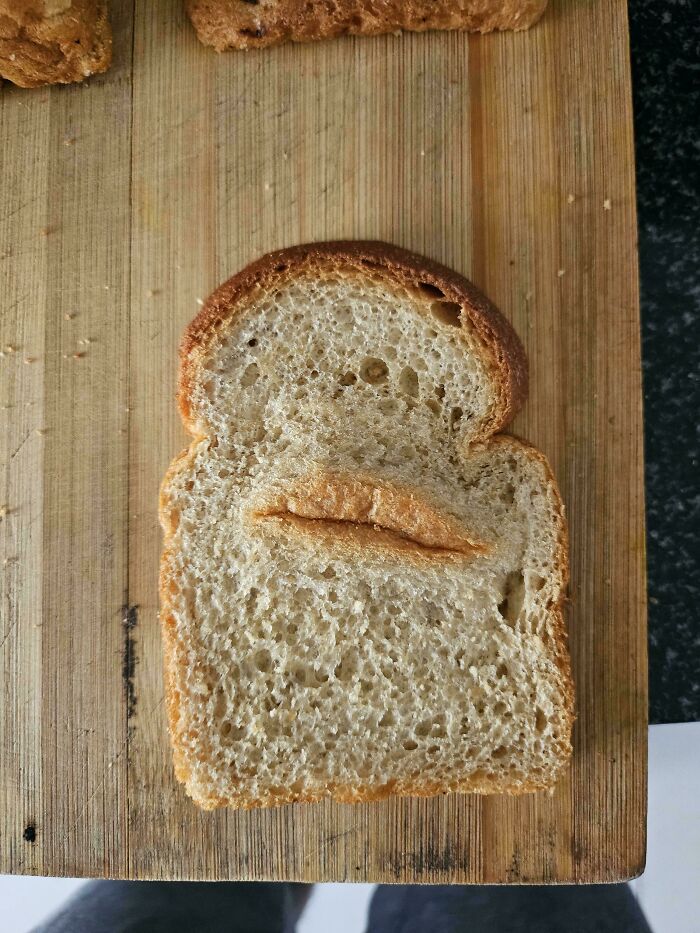 Slice of bread with a crusty line resembling lips on a wooden cutting board, a mildly interesting find shared online.