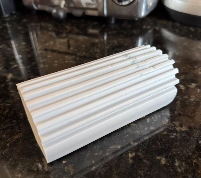 Cleaning tool with ridged surface designed for spotless grout line maintenance on a dark kitchen countertop.