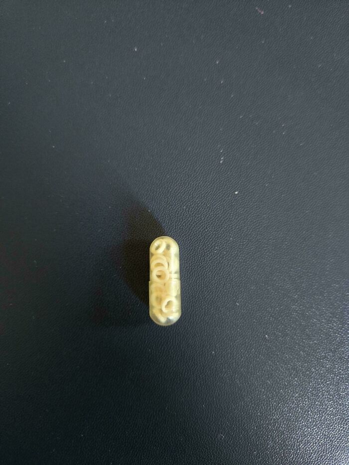 Capsule filled with tiny alphabet-shaped pasta on a dark surface, seen in a mildly interesting way.