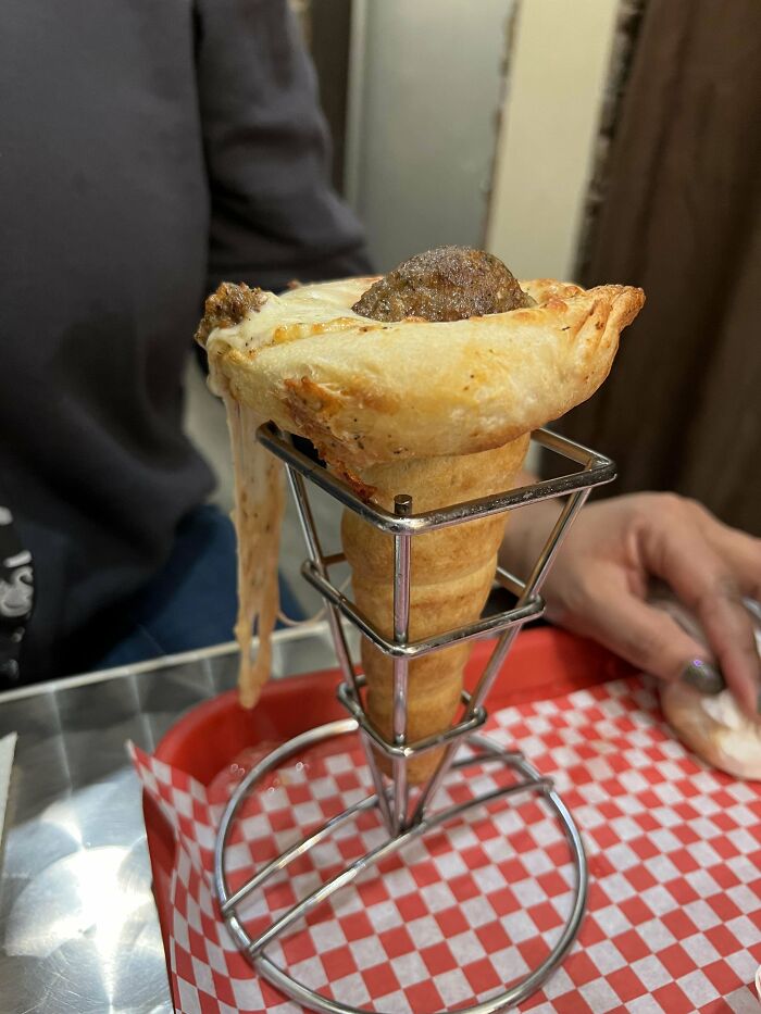 Pizza cone with meatball and melted cheese served in an unusual way on a metal stand, showcasing unholy meal presentation.