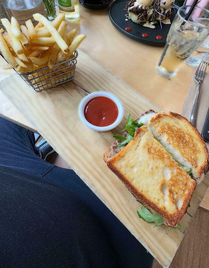 Unholy meal presentation with fries in a small basket and a sandwich served on a wooden board with ketchup.