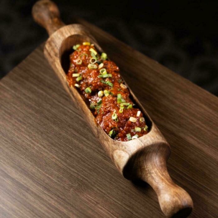 Unholy meal presentation of meatballs served inside a hollow wooden rolling pin, garnished with chopped green onions.