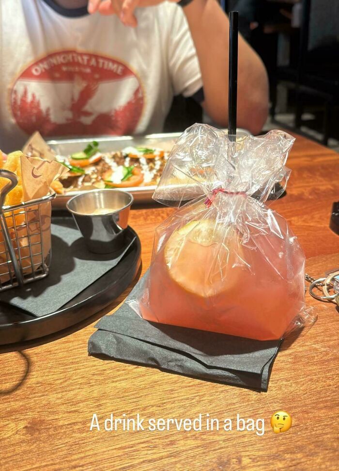 A drink served in a plastic bag with a straw, alongside a meal, showing unholy meal serving creativity.
