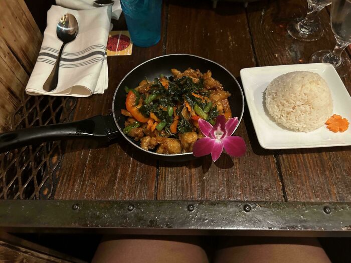 Meal served in a frying pan with vegetables and rice on a rustic wooden table, showcasing unholy meal presentation.