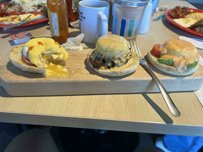 Three unusual small sandwiches with different sauces served on a wooden board, highlighting unholy meal presentation.