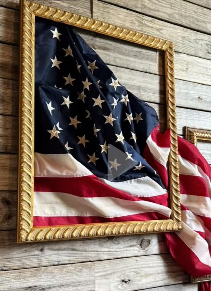 American flag folded oddly inside a gold frame on a wooden wall, showcasing a horrible craft attempt by netizens.